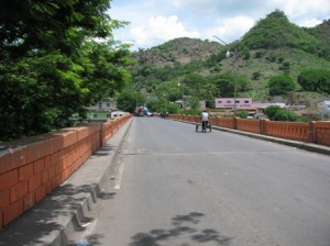 Picture of the long bridge which separates the two countries. The road is empty apart from a small cycle rickshaw.