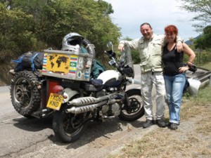 Picture of Andy and Maya stood beside their Triumph. Andy has his arm around Maya and they are both smiling.